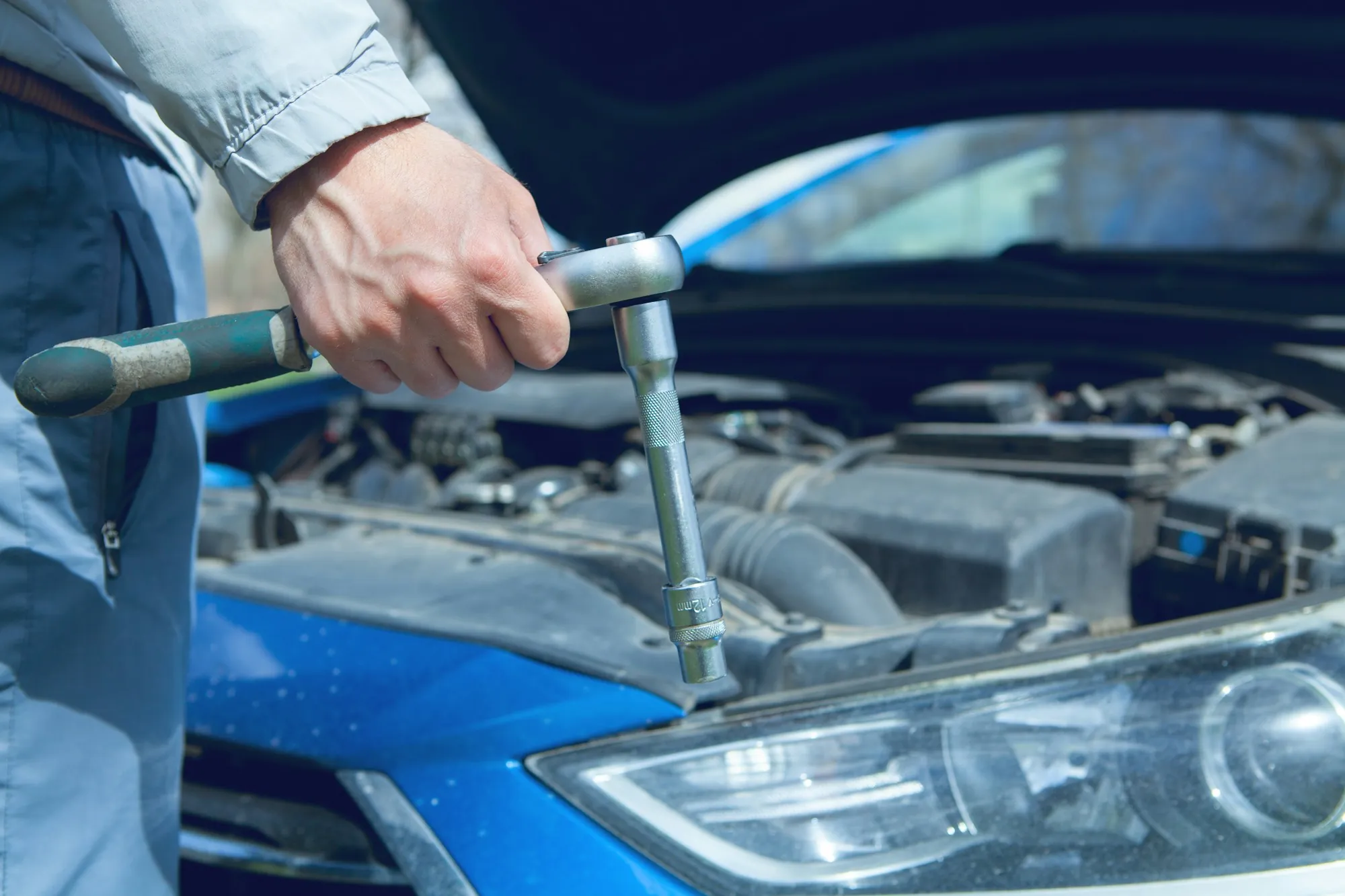 Hand turning a wrench under the hood of a blue car
