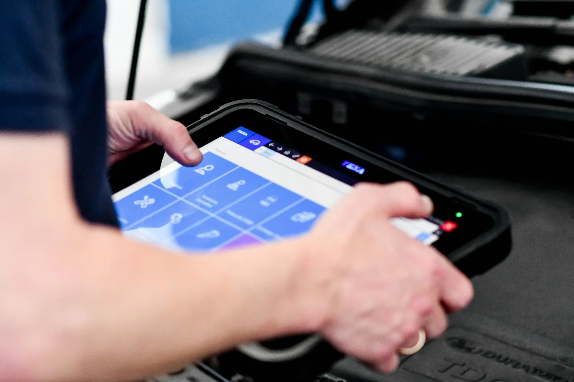 Close view of a hand holding a tablet scan tool near a vehicle