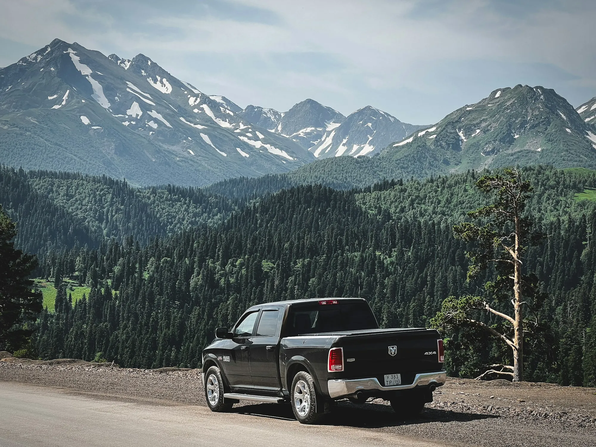 Black pickup truck on a mountain pass road with forested peaks